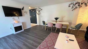 Un salon moderne doté d’un téléviseur à écran plat, d’un coin repas avec une table et des chaises, et d’un tapis à motifs.