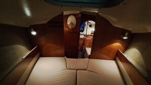 Cabina de barco con cama central, paredes de madera y una pequeña ventana.