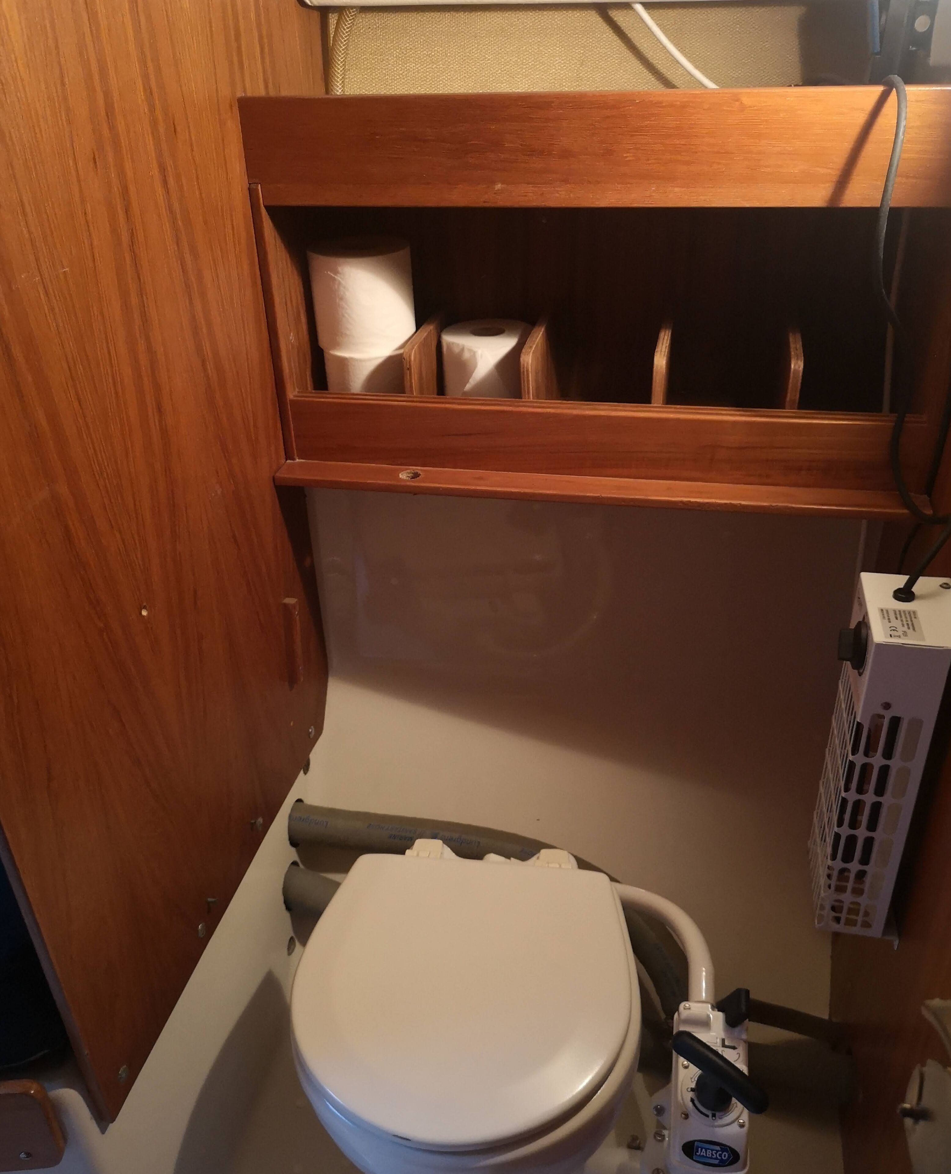 Une petite salle de bain avec des toilettes blanches, un meuble en bois au-dessus du lavabo et un porte-brosse pour les toilettes de la marque JABISCO.