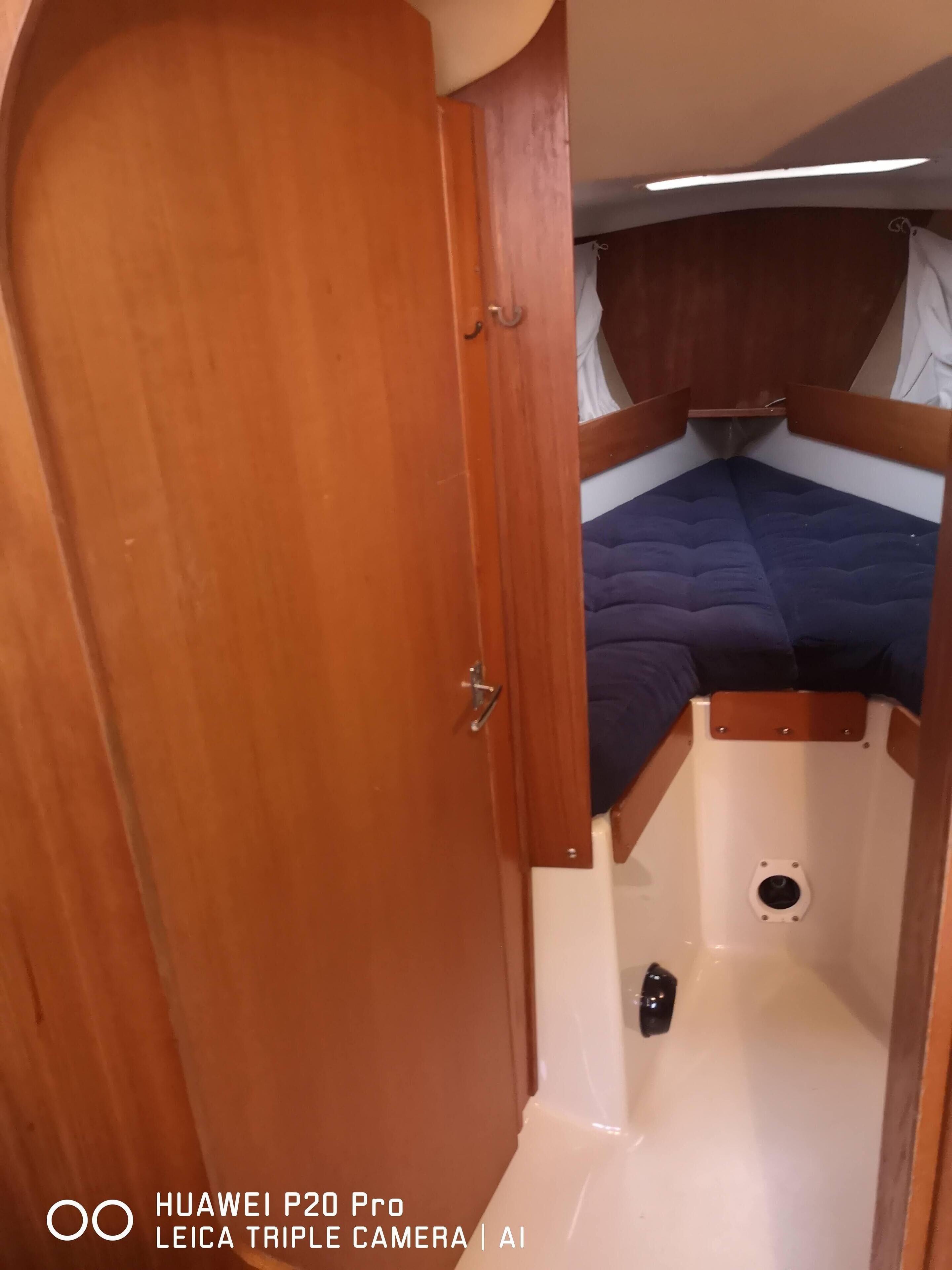 A compact, well-lit cabin with a wooden door, a small seating area with a blue cushion, and a white floor.