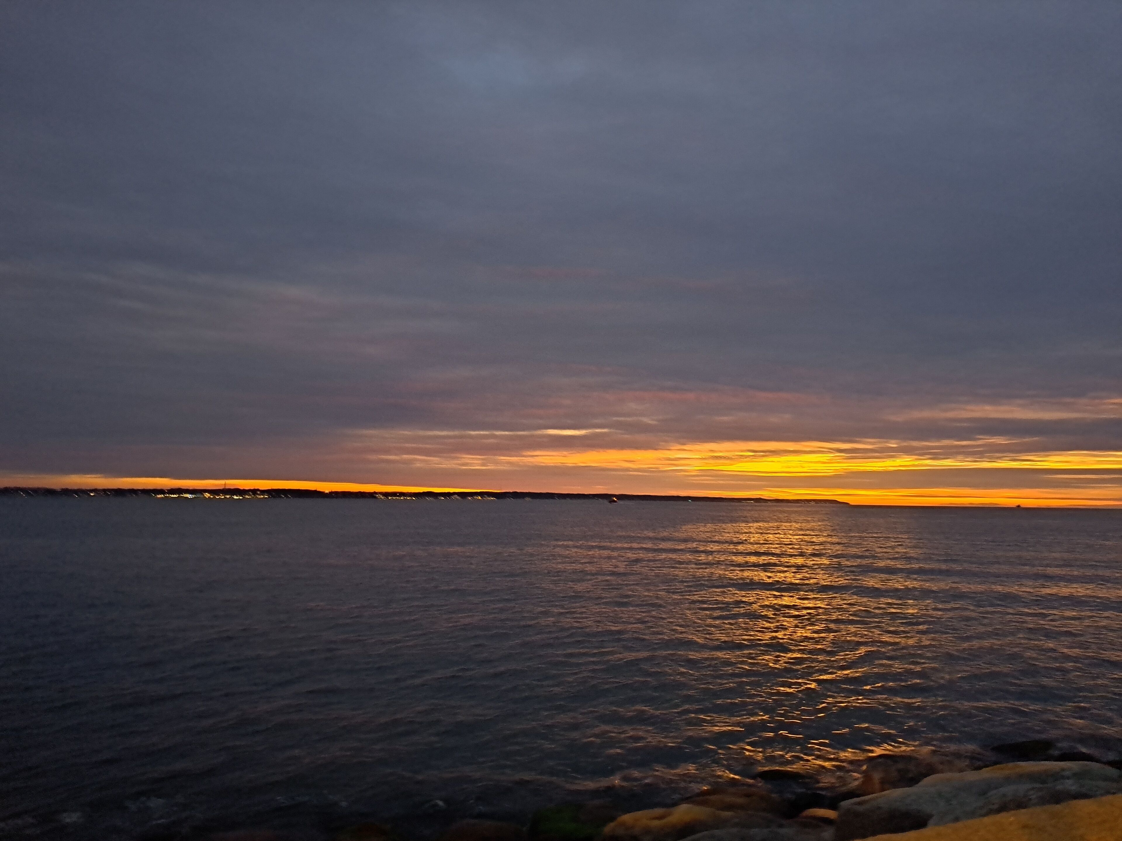 A sunset over a calm sea with a rocky shoreline.