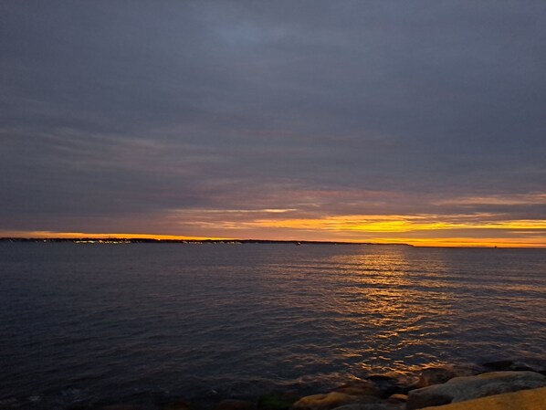 Auringonlasku tyynen meren yllä, horisontissa kivinen rantaviiva.