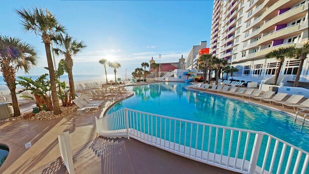 A resort pool with a view of the beach and ocean, surrounded by palm trees and lounge chairs. - 1BD Suite/Daytona - Ocean Walk Guest Suite!! (Daytona Beach)