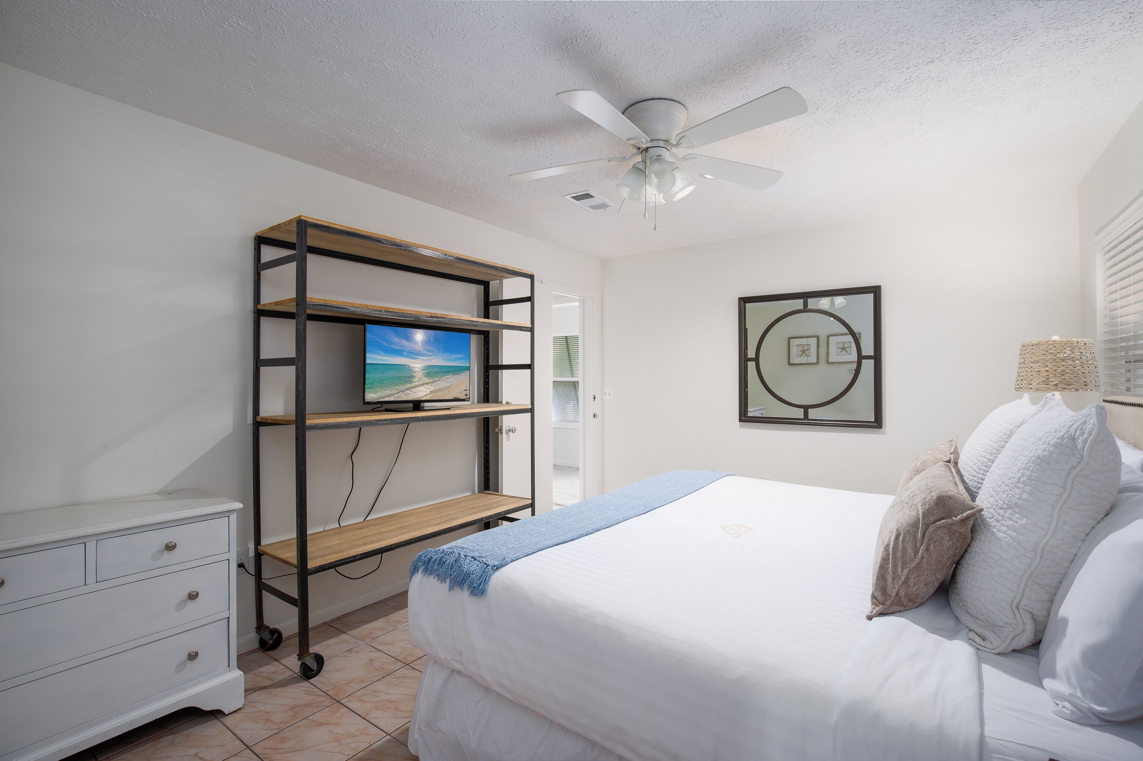A bedroom with a bed, a TV on a shelf, a ceiling fan, and a framed picture on the wall.