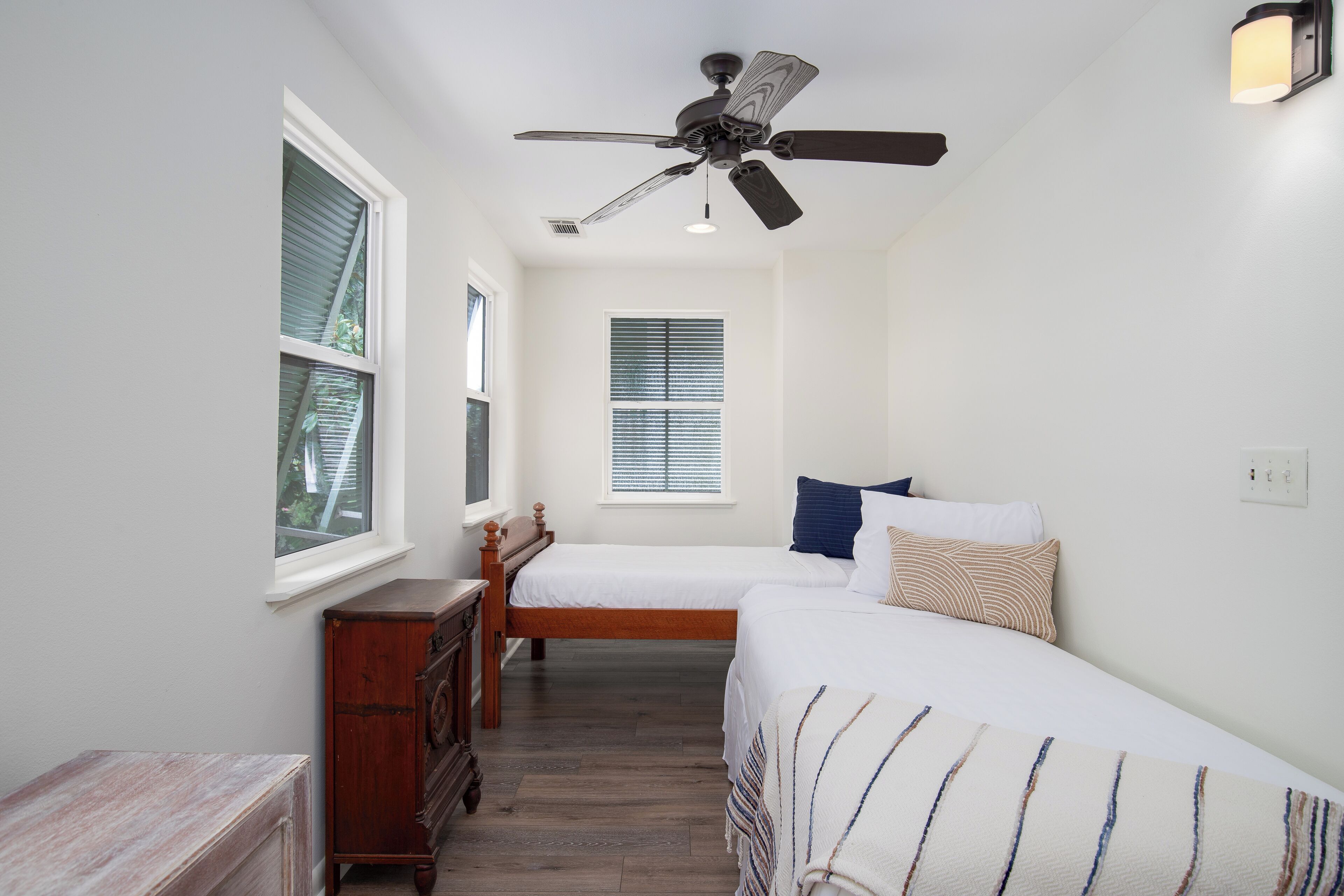 Une chambre avec deux lits, un ventilateur de plafond et une fenêtre avec des stores.