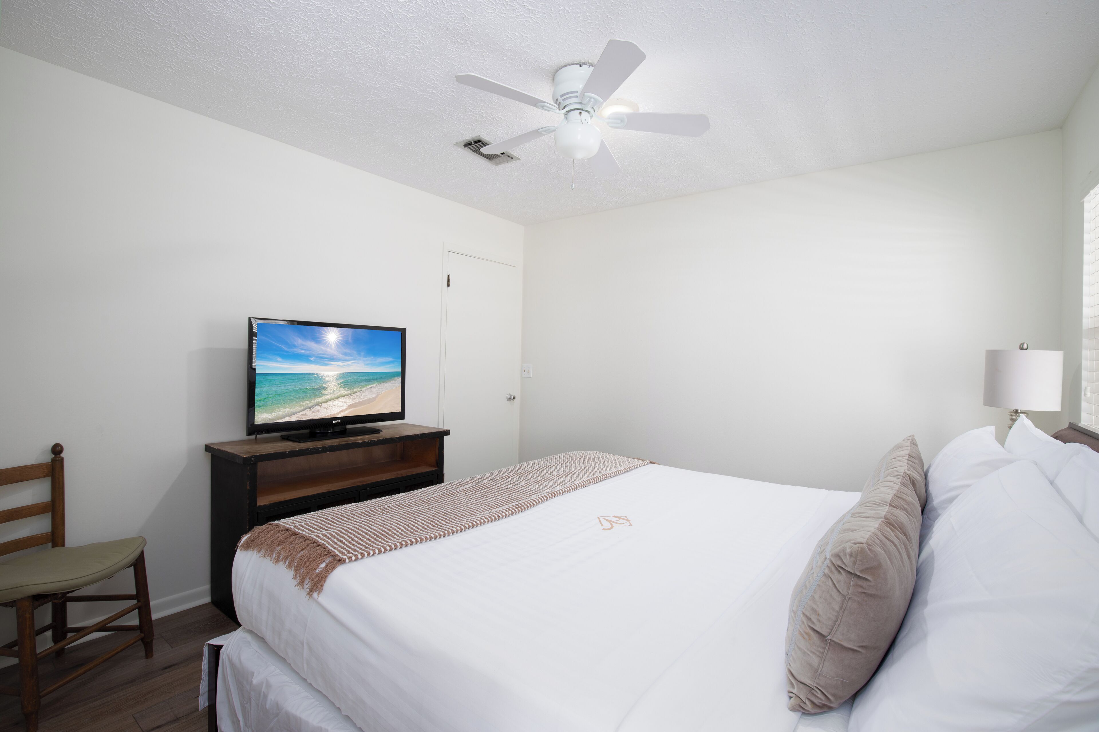 Une chambre d’hôtel avec un lit, un téléviseur posé sur un meuble en bois, un ventilateur de plafond et une fenêtre avec des stores.