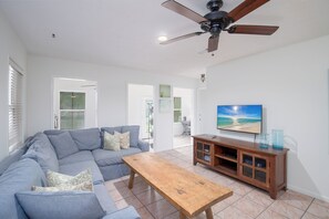 A living room with a sectional sofa, a wooden coffee table, a TV on a wooden stand, and a ceiling fan.