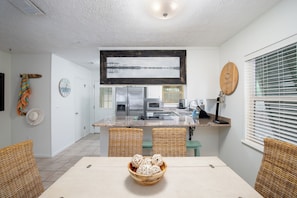 A modern kitchen with a central island, wicker chairs, and a dining table with a bowl of decorative items.