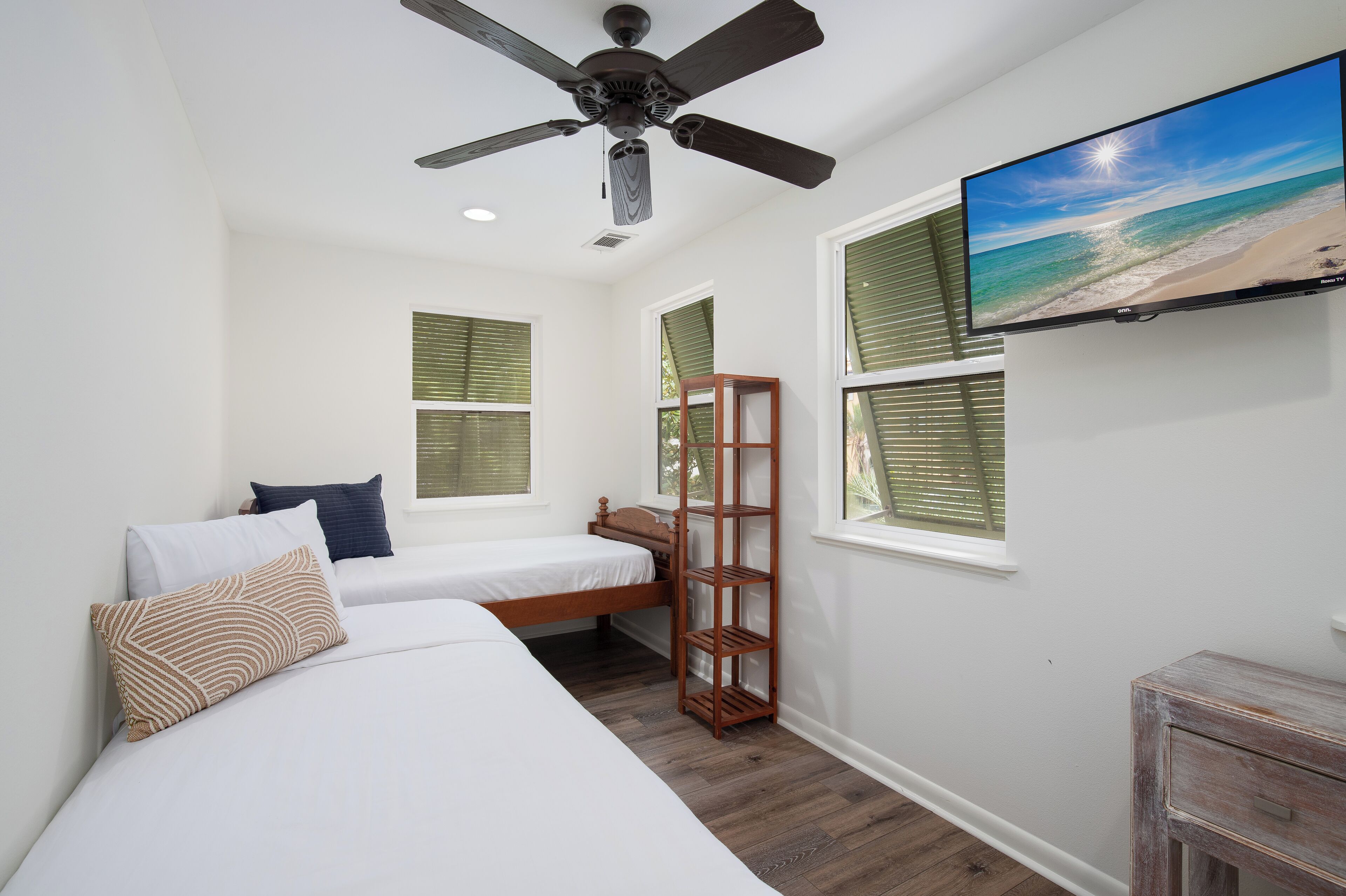 A bedroom with two beds, a ceiling fan, a TV on the wall, and a window with blinds.