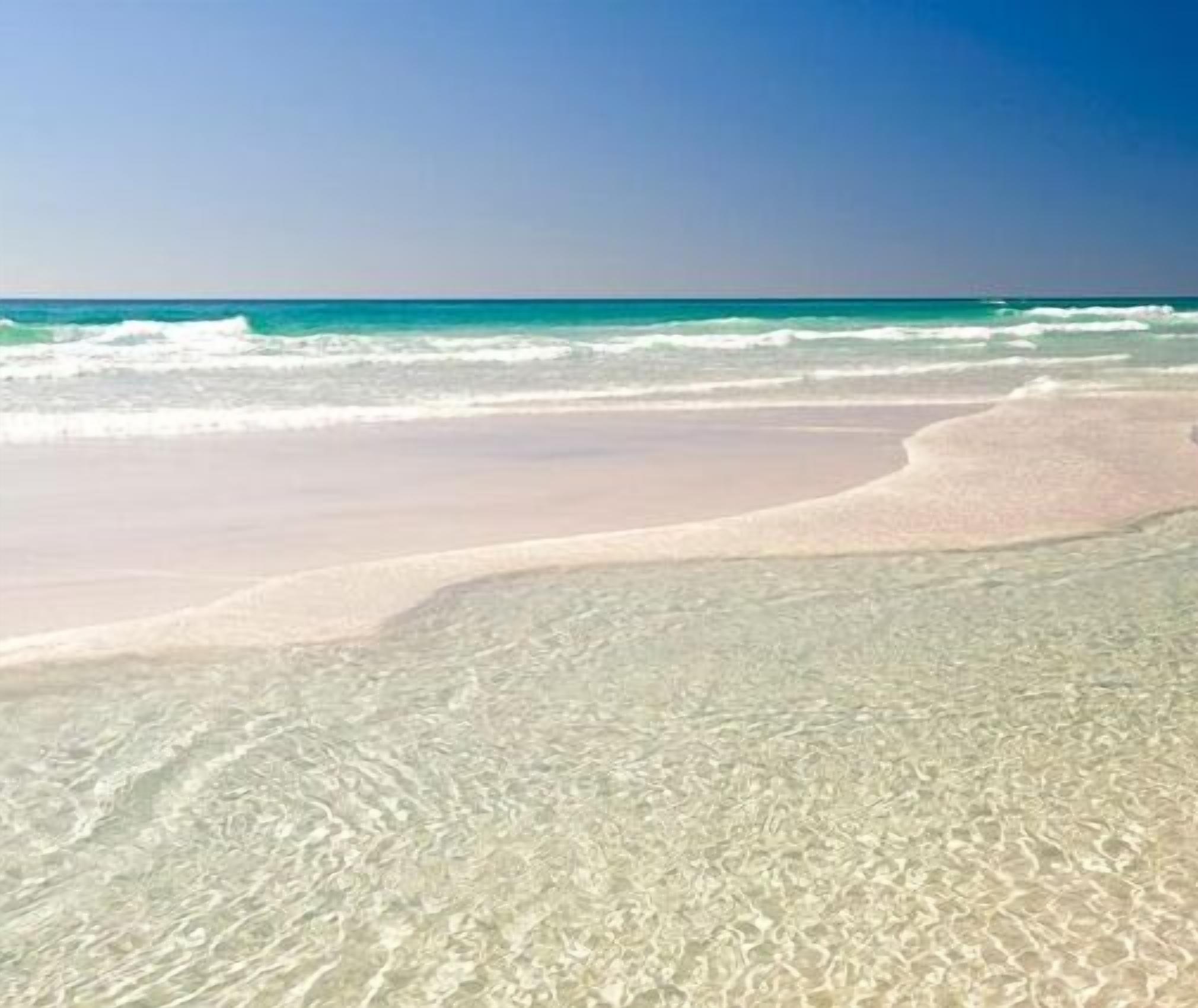 A beach with clear shallow water and a sandy shore.