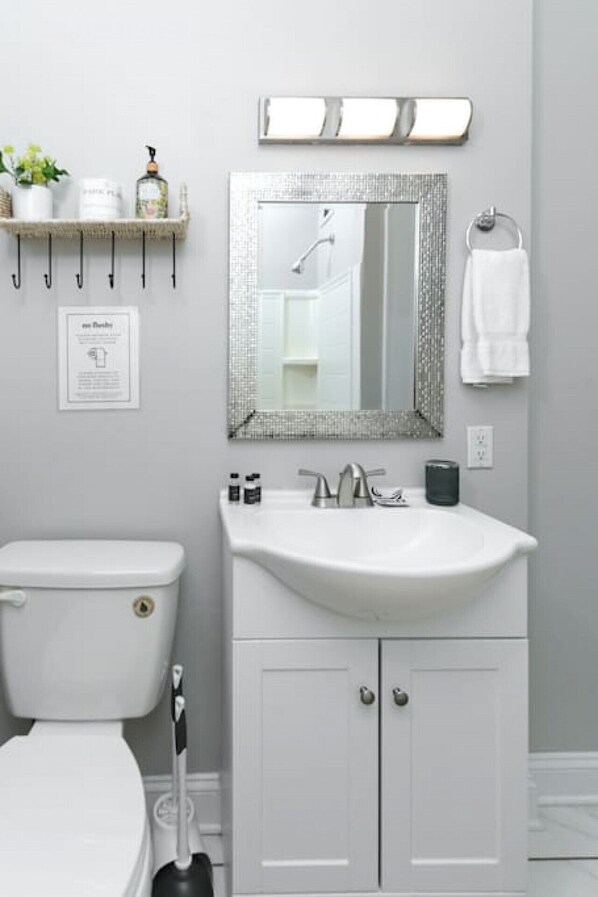 A bathroom with a white toilet, a sink with a mirror above it, and a towel hanging on a rack. - Revamped 3BR Oasis on Forest Dr (Columbia)