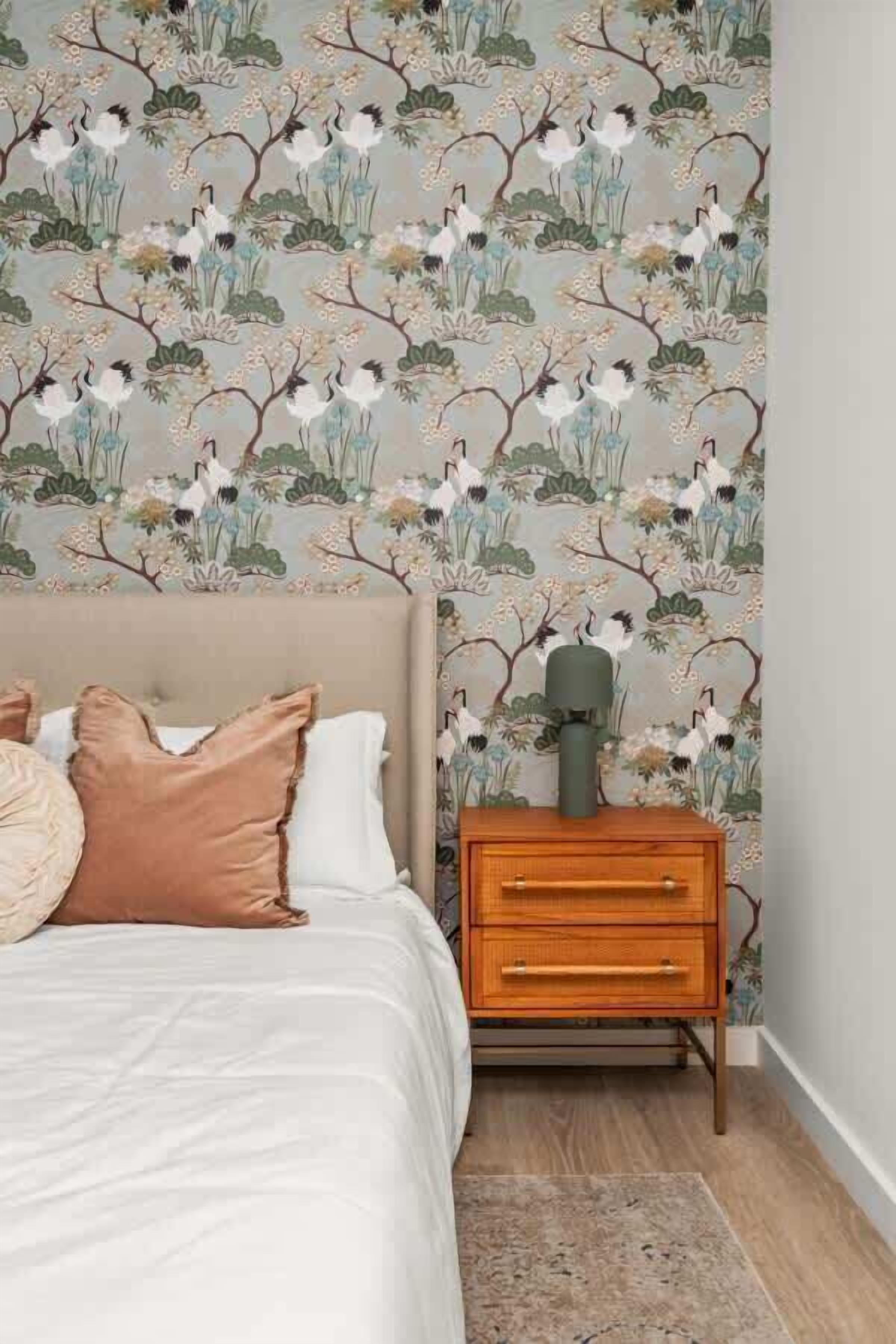 A bedroom with a bed, pillows, a nightstand, and a wall with floral wallpaper.