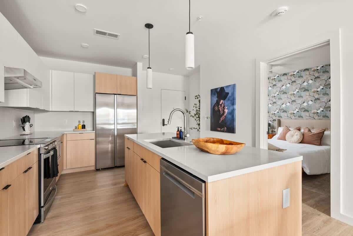 A modern kitchen with a central island, stainless steel appliances, and a wooden bowl on the countertop.