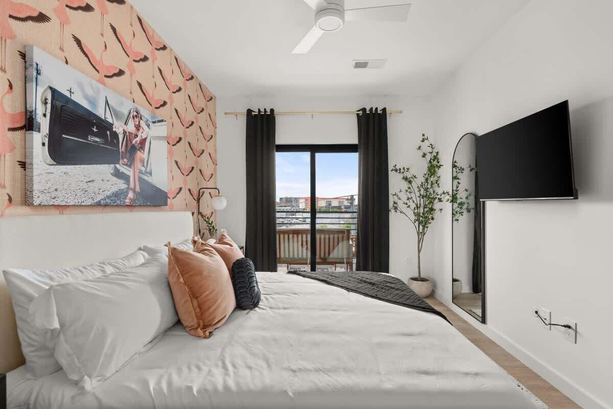 A bedroom with a bed, a TV, a window with curtains, a plant, and a balcony view.