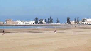 Une vaste plage de sable où se trouvent quelques personnes, et, au loin, une structure qui ressemble à un château.