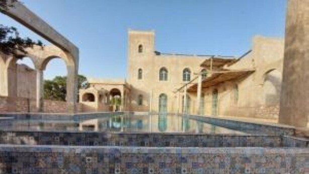 Une piscine bordée de carreaux, un bâtiment doté d’arches et d’une tour, et un ciel dégagé.
