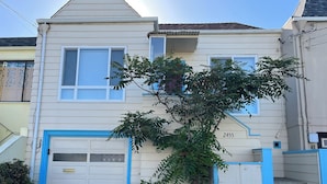 A two-story house with a garage, a tree in front, and a blue gate.
