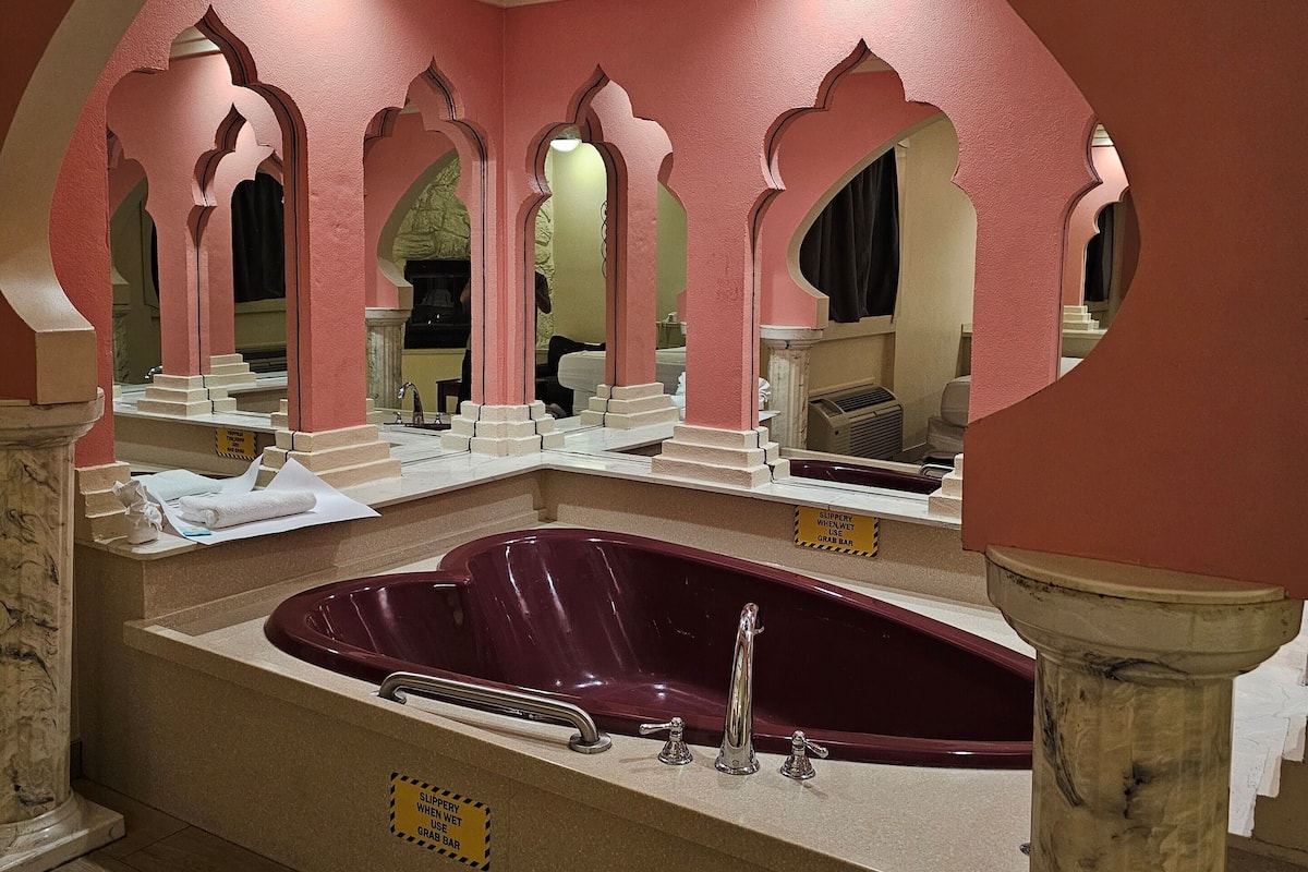 Un baño con una bañera grande, varios espejos y arcos.