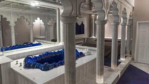 A bathroom with marble countertops, a blue glass sink, and columns with ornate capitals.