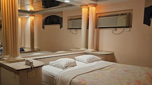A hotel room with a bed, bedside tables, a mirror, an air conditioning unit, and a telephone.