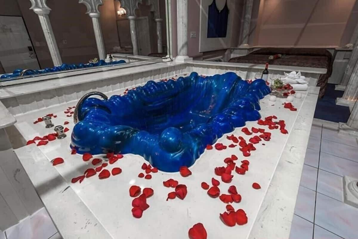 Una habitación con un gran adorno azul decorativo, pétalos de rosa roja esparcidos y una cama con cubrecama oscura.
