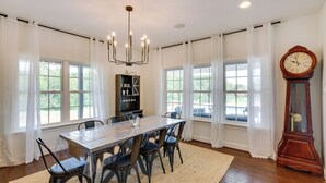 Comedor con una mesa grande, sillas, candelabro, reloj y ventanas amplias con cortinas.