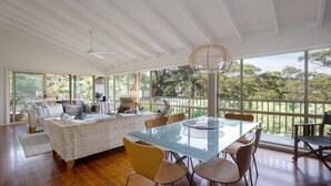 Quarto espaçoso com uma grande mesa de vidro, móveis de vime e vista para as árvores através de amplas janelas.