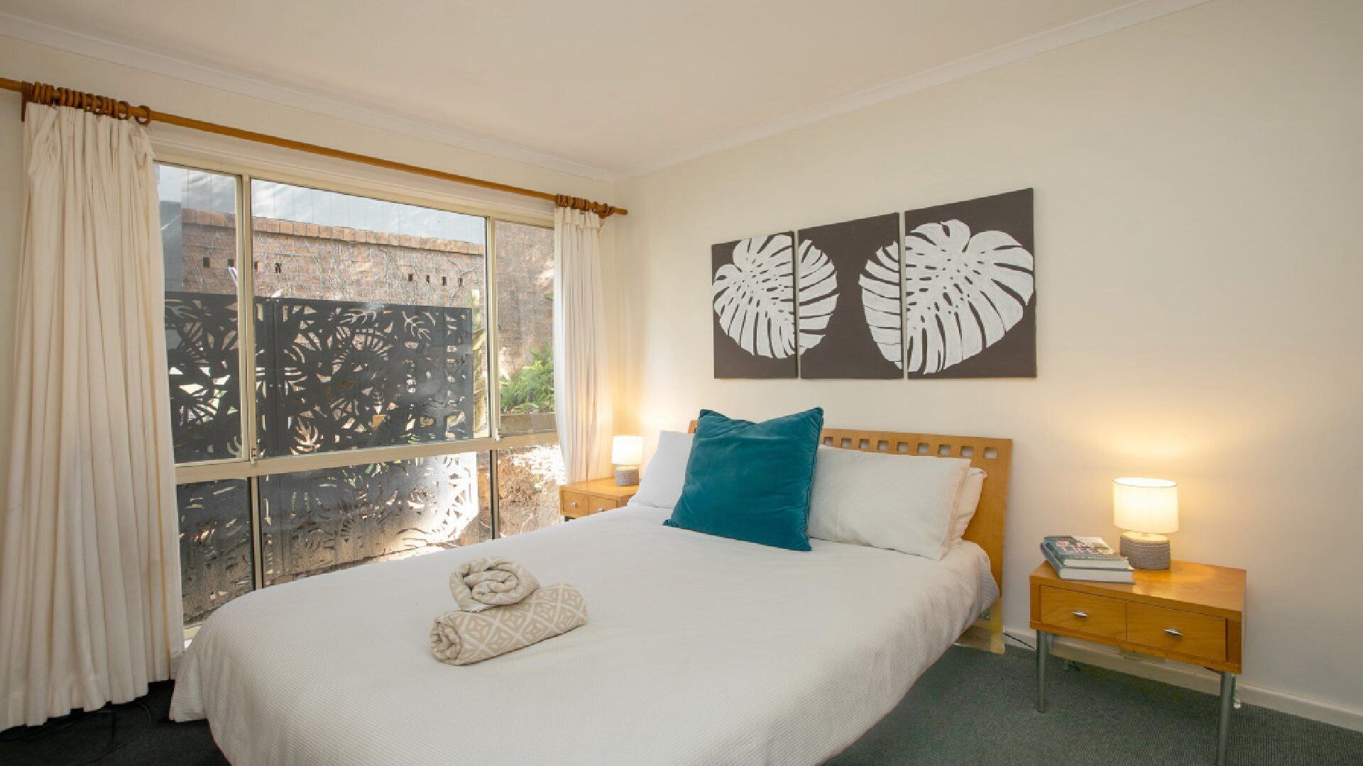 A neatly made bed with a rolled towel, two pillows, and a nightstand with a lamp.
