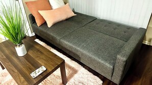A small, neatly arranged room with a sofa, a small table, a potted plant, and a window with blinds. - Eagle Stay 7 Condo-Eagle Pass (Eagle Pass)