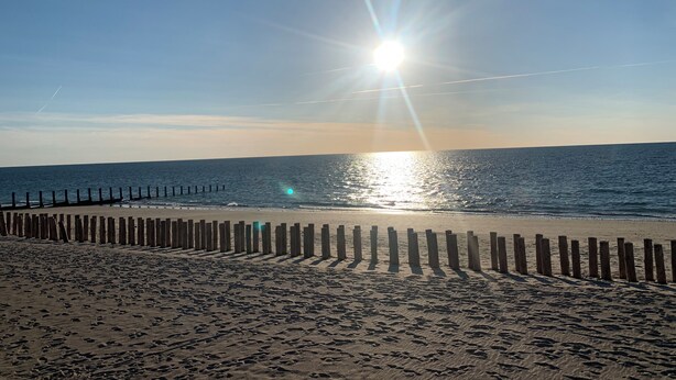 Une plage avec une clôture en bois et des empreintes de pas dans le sable.