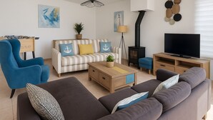Un salon avec un canapé à rayures, un fauteuil bleu, un canapé gris, une table basse, un meuble pour la télévision, une cheminée et des œuvres d’art mural.
