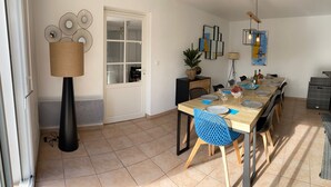 Un coin repas avec une table en bois dressée pour six personnes, entourée de chaises bleues, d’un grand lampadaire et d’œuvres d’art murales.