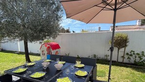 Un espace extérieur aménagé pour les repas, avec une table dressée pour quatre personnes, entourée de chaises en osier.