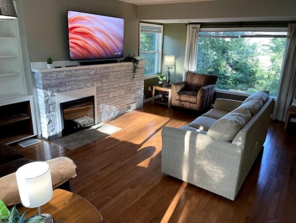 A living room with a fireplace, a sofa, a TV, and a view of greenery outside.