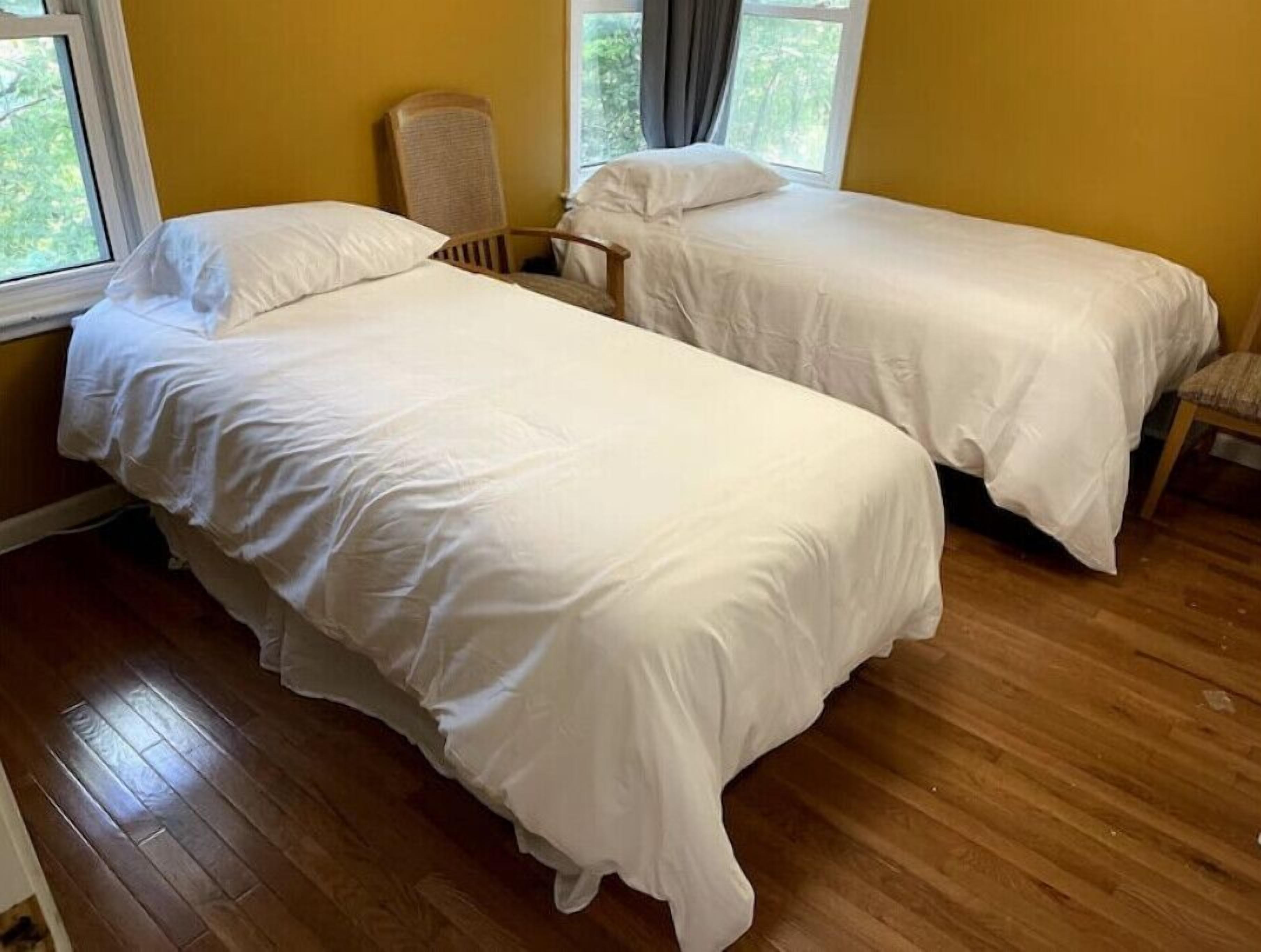 A room with two single beds, wooden flooring, and a chair.