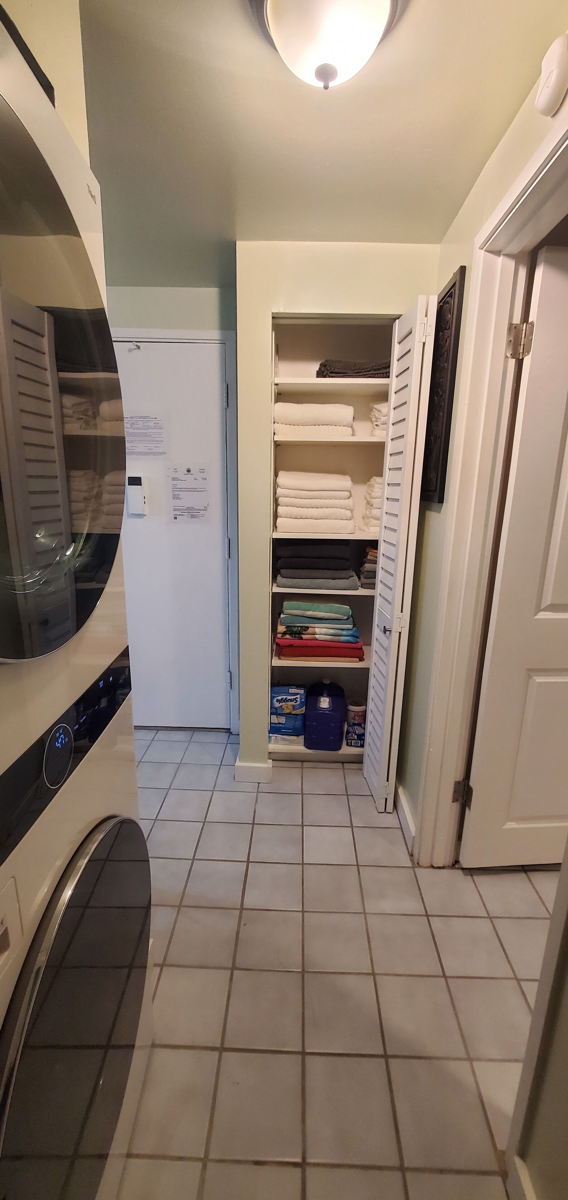 A compact kitchen with a built-in washer, a refrigerator, and a storage closet with shelves.