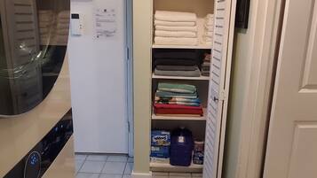 A compact kitchen with a built-in washer, a refrigerator, and a storage closet with shelves.