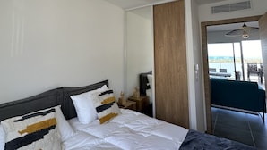 A modern hotel room with a large bed, a ceiling lamp, a wooden door, and a view of the sea. - new luxury residence (1 bedroom) Sea view, Citadel and port of Calvi (Calvi)
