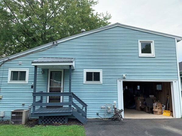 A light blue two-story house with a front porch, a garage, and a small outdoor area with a lawnmower.