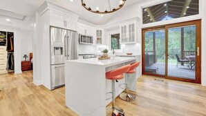 A modern kitchen with white cabinetry, stainless steel appliances, and a large island with bar stools. - Blue Water Dunes Cottage (Tiny)