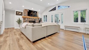 A spacious living room with a stone fireplace, a large sofa, and a wooden floor. - Blue Water Dunes Cottage (Tiny)
