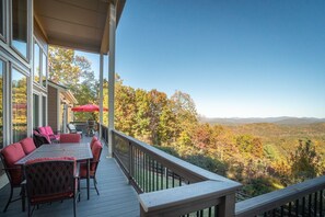 Une terrasse extérieure couverte, dotée d’une table et de chaises, qui offre une vue sur une vallée boisée.