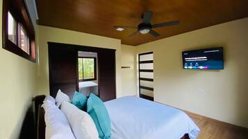 Un dormitorio con cama, almohadas, ventilador de techo, televisión y ventana.