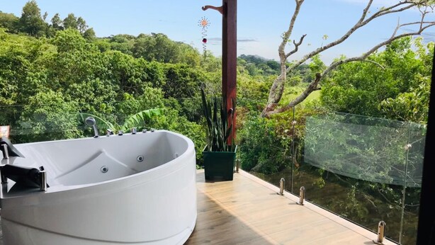 A modern bathroom with a large freestanding bathtub, wooden flooring, and a view of lush greenery.