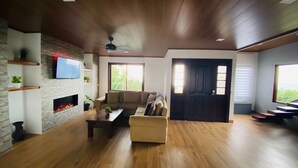 A spacious living room with a fireplace, a sofa, and a coffee table. There is a television mounted on the wall and a door leading to another room.