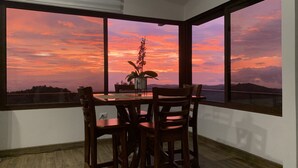 A dining area with a table and chairs, a potted plant, and a view of a sunset over a landscape.