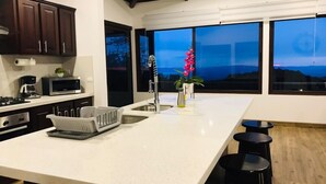 A modern kitchen with a large island, dark wood cabinets, and a view of the mountains through large windows.
