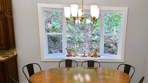 A dining area with a round wooden table surrounded by chairs, a chandelier, and a window with a view of greenery. - Mountain Ridge Retreat - Private & Peaceful Getaway. Family & Pet Friendly (West Park)