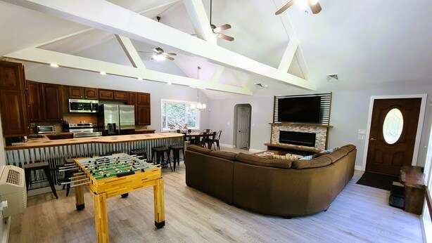 A spacious living area with a foosball table, a large brown sectional sofa, a flat-screen TV mounted on a stone fireplace, and a kitchen with modern appliances. - Mountain Ridge Retreat - Private & Peaceful Getaway. Family & Pet Friendly (West Park)