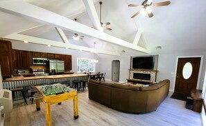 A spacious living area with a foosball table, a large brown sectional sofa, a flat-screen TV mounted on a stone fireplace, and a kitchen with modern appliances. - Mountain Ridge Retreat - Private & Peaceful Getaway. Family & Pet Friendly (West Park)